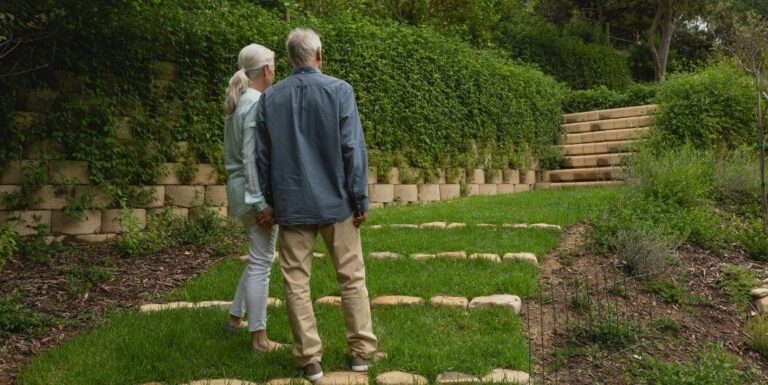 Elderly Couple Walking Through Bright Hallway With Clear Signs At Assisted Living Facility