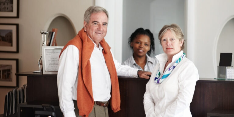 Two Elderly Residents Smiling Beside Staff Member at a Reception Desk in an Independent Living Facility